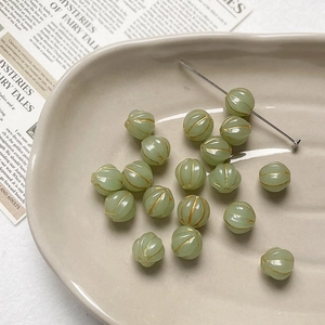 Close-up of vintage light green pumpkin beads with gold accents on a ceramic tray
