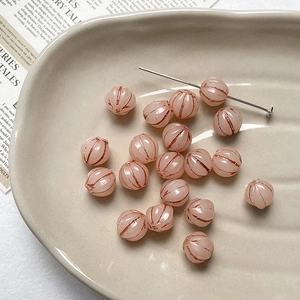 Close-up of pink pumpkin beads with gold accents on a ceramic tray for DIY jewelry