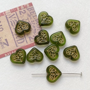 Macro shot of green heart-shaped glass beads with gold floral pattern and threading pin