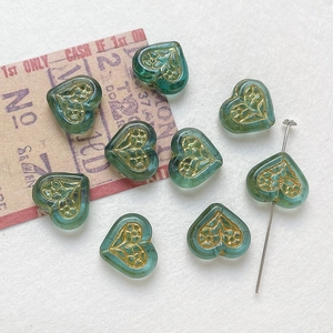 Detailed view of teal heart glass beads with golden floral patterns for DIY jewelry