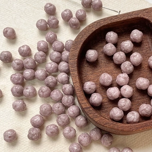 Macro shot of 8mm mauve Czech glass beads with detailed rose carving for DIY jewelry