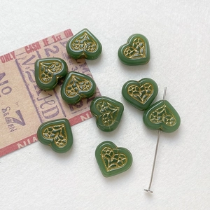 Macro shot of dark green heart glass beads with gold floral details and straight hole view