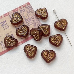 Detail of vintage heart-shaped amber glass beads with golden floral engraving for DIY jewelry