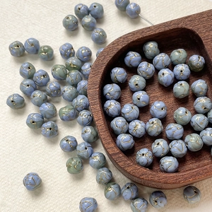 Macro view of 8mm blue Czech glass beads with golden floral etchings for DIY jewelry