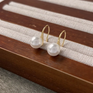 Élégantes boucles d'oreilles crochet dorées avec perles blanches rondes sur un plateau
