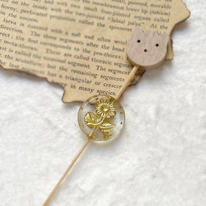Detail of transparent resin bead with golden sunflower and wooden cat head pin