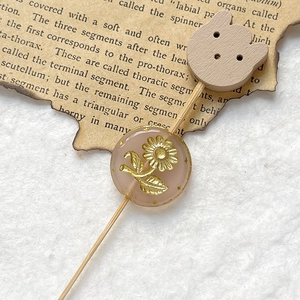 Detailed close-up of a pink translucent bead with gold sunflower engraving on a wood pin