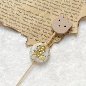 Macro shot of retro etched glass bead with gold sunflower motif on a wooden hair stick