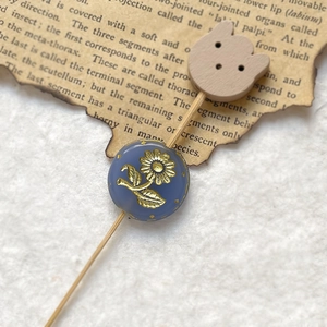 Macro shot of vintage blue Czech glass bead with gold floral engraving on paper background
