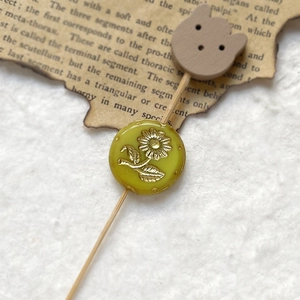 Detail of a yellow round bead with gold floral relief and a wooden bear charm ornament