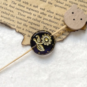Macro detail of a vintage purple glass bead with gold floral relief and celestial pattern