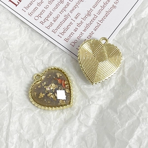 Macro shot of heart-shaped DIY charms with gold foil, dried flowers, and textured metal back