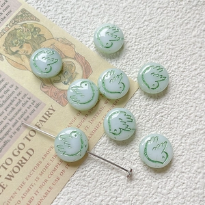 Detail of green glass beads with bird engraving and silver metal needle for DIY jewelry