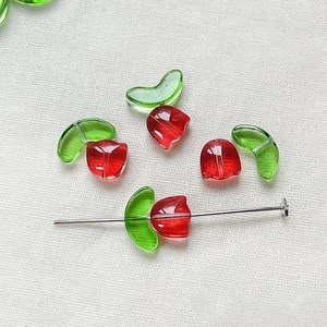 Macro shot of tulip-shaped glass beads with red petals and green leaves for DIY jewelry