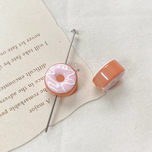 Close-up of orange donut glaze resin bead with pink and white swirl pattern for DIY jewelry