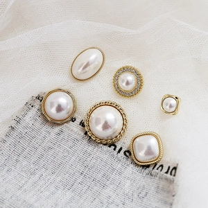 Detailed view of six assorted geometric faux pearl and silver earring charms on lace fabric