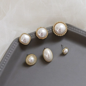 Detailed close-up of vintage geometric pearl earrings on a textured gray tray display