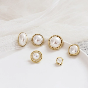 Detail of 925 silver pearl earrings with geometric gold frames on white lace background