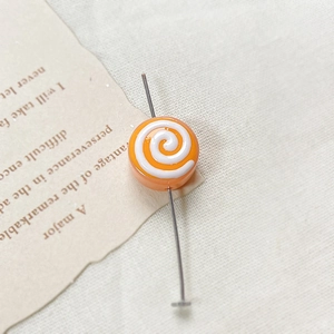 Close-up of orange spiral glazed doughnut bead on a metal pin for DIY jewelry making