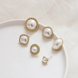 Detail of assorted geometric pearl earrings with gold frames on white ceramic tray