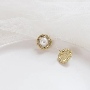Detail of gold pearl earrings with rhinestone halo and silver pins on white mesh background
