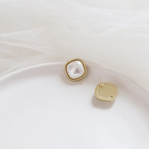 Detailed close-up of square pearl earrings with textured gold metal frame on soft fabric