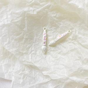 Detailed close-up of white paint brush alloy pendants with pink floral motifs for DIY jewelry