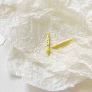 Detail of two yellow enamel paintbrush charms for DIY jewelry making on white paper