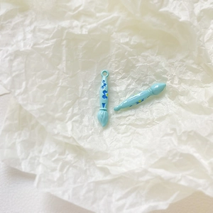 Detailed close-up of light blue paintbrush charms with floral patterns for DIY jewelry