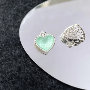 Detail van mintgroene hartvormige hanger en zilveren gehamerde bedel voor DIY sieraden