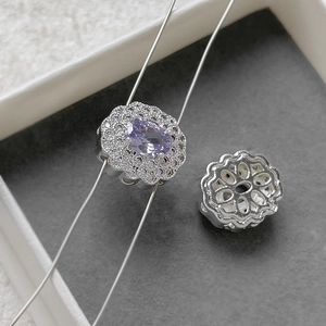Macro detail of a silver floral charm featuring an oval purple stone with double halo diamonds
