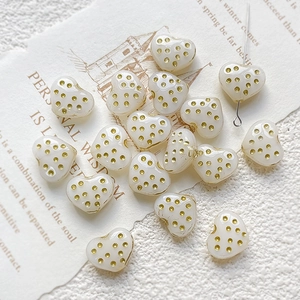 Macro detail of heart-shaped cream beads with gold polka dots for DIY jewelry making