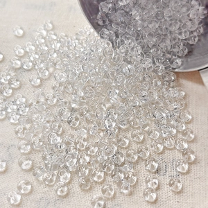 Macro view of 4mm transparent mushroom-shaped glass beads scattered on beige fabric