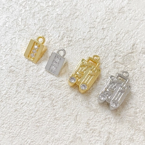 Macro shot of 18k gold plated suitcase and cheese charms with zircon stone details