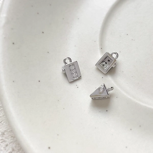 Macro shot of silver suitcase and cheese slice charms with cubic zirconia inlay details