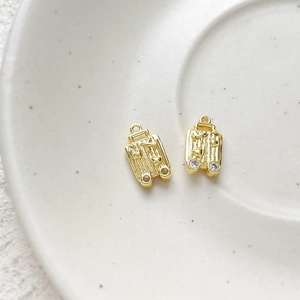 Macro detail of gold-plated suitcase charms with heart relief and zircon wheels