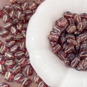 Detail of dark red glass tulip beads with gold edges on dark wood surface