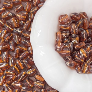 Macro shot of amber tulip glass beads scattered on wood surface and ceramic plate