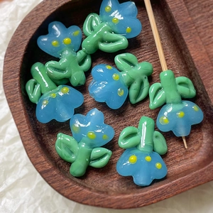Macro detail of handmade light blue flower glass beads with green leaves on wood