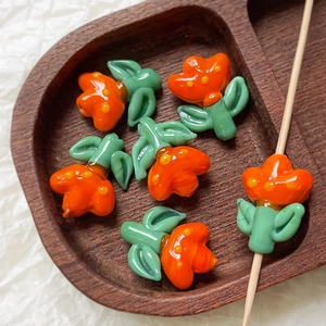 Macro shot of orange tulip glass beads for DIY jewelry making with green leaves