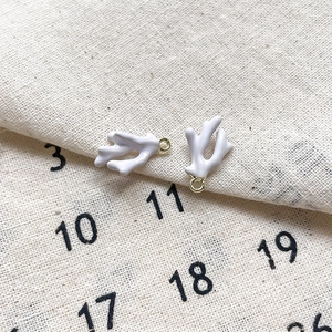 Gros plan de breloques en corail émaillé blanc avec anneaux dorés pour bijoux DIY