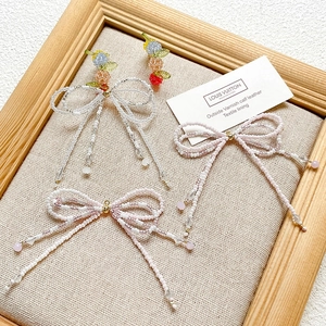 Detail of handmade beaded bow earrings with colorful fruit-inspired beads on canvas