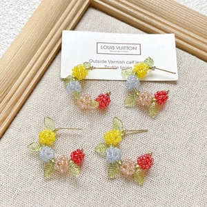Handmade colorful seed bead C-shaped hoop earrings with floral charms on linen background