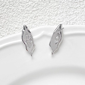 Detalle de pendientes irregulares plateados con circonita y lazo para joyería artesanal