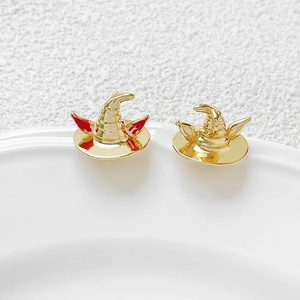 Macro shot of gold-plated wizard hat stud earrings with red enamel on white ceramic