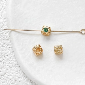 Macro detail of 18k gold plated cube beads with green zircon and hammered metal texture