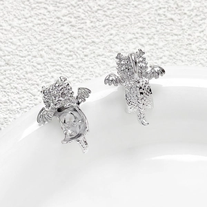 Macro shot of silver dragon earrings with sparkling cubic zirconia on white ceramic tray