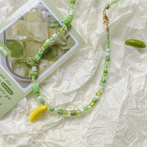 Handmade beaded necklace with yellow banana pendant and green glass beads on white paper