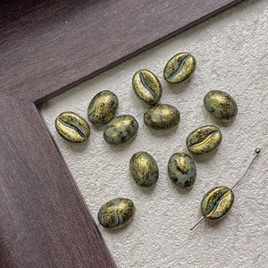 Detail of coffee bean shaped glass beads with vintage blue and gold leaf texture for DIY craft