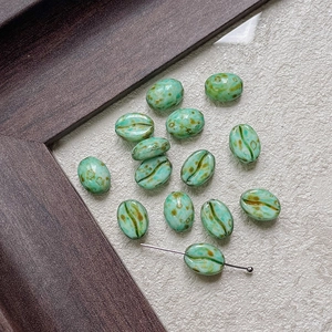 Detailed view of light green coffee bean-shaped glass beads with brown spots for DIY jewelry